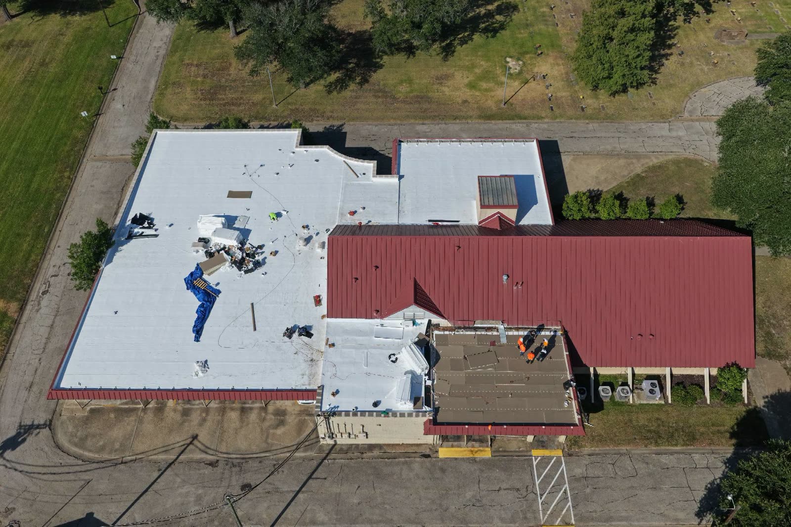 Aerial view of a white flat commercial roof and a red metal roof with a crew